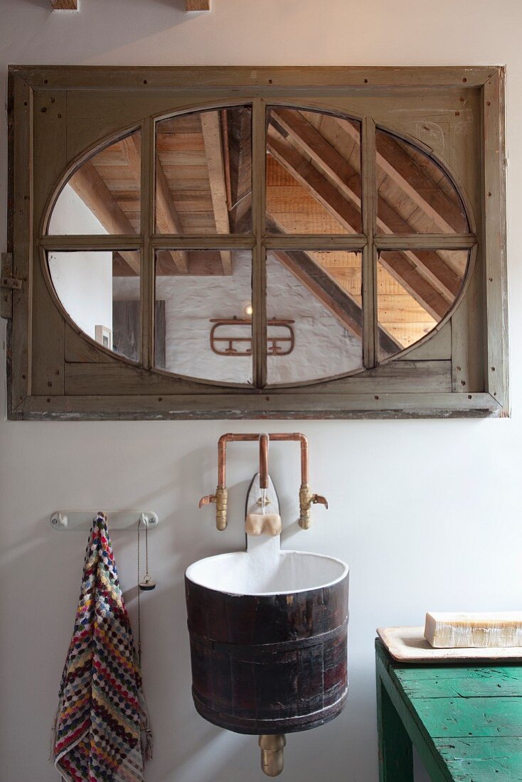Sink made from wooden tub mounted on wall below lattice window with wooden frame