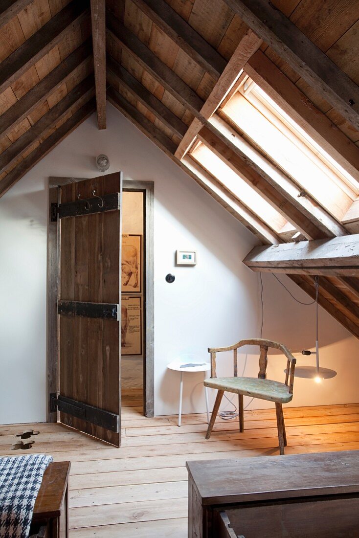 Rustikales Zimmer mit sichtbarem Dachstuhl, schlichter Armlehnstuhl unter Dachfenster