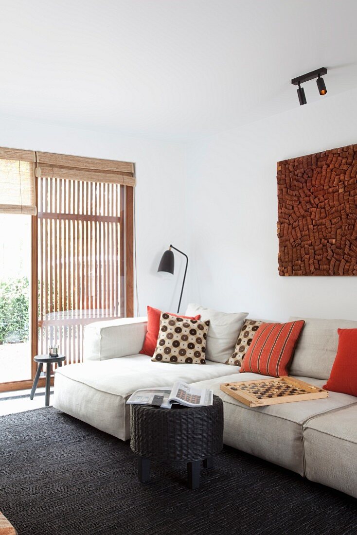 Moderne Wohnzimmerecke mit hellem Polstersofa und gemusterten Kissen, im Hintergrund Terrassentür mit Holzlamellen-Element