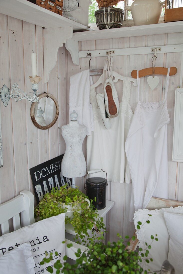 White rustic clothing hung on clothes hangers on white-stained wooden wall