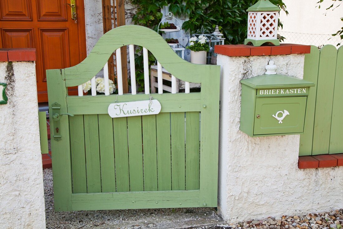 Grün lackiertes Holz Gartentürchen mit Namensschild, neben Mauerstück mit aufgehängtem Briefkasten in gleicher Farbe