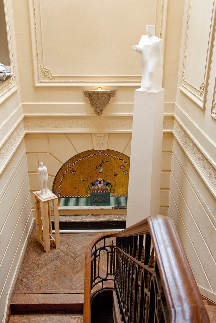 View down staircase: sculpture on plinth on landing against gilded arch in Art-Nouveau wall