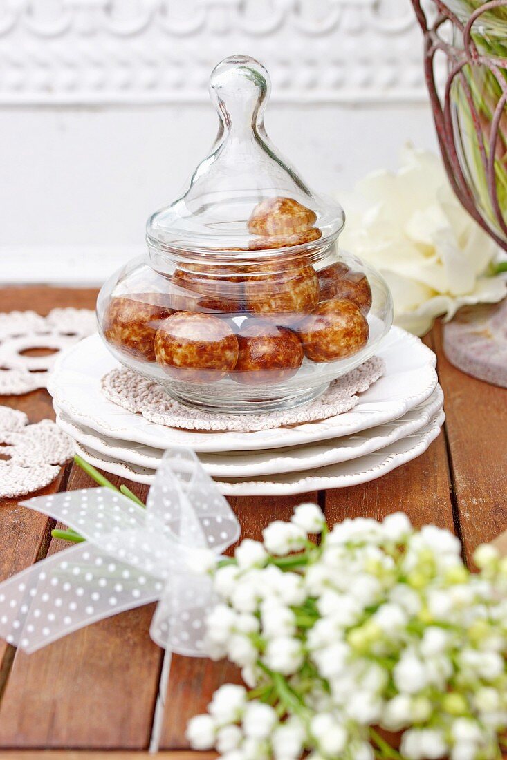 Sweets in glass jar with lid and bouquet of lily-of-the-valley in foreground
