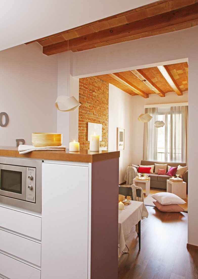 Moderne Küchentheke in offenem Wohnraum, im Hintergrund Loungeecke unter Holzbalkendecke