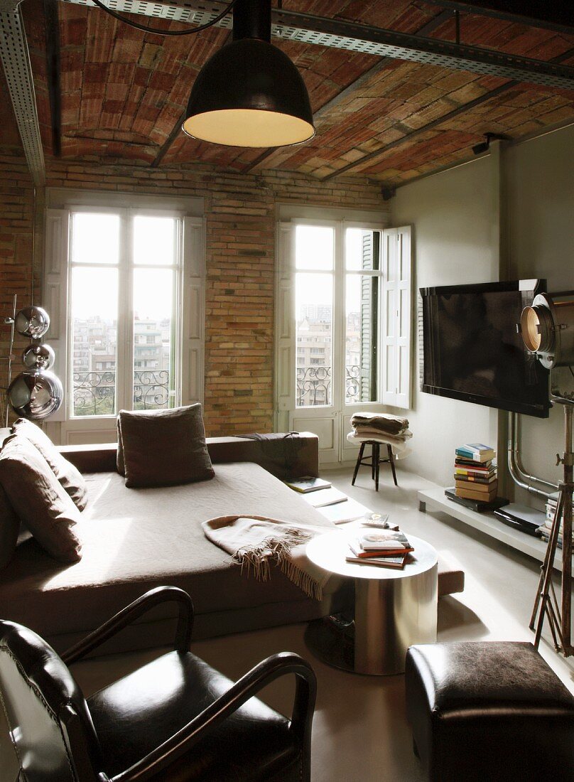 Wohn-Schlafbereich mit Sessel und Hocker neben Bett, gegenüber Flachbildfernseher an Wand aufgehängt, in rustikalem Ambiente mit Ziegelwand und -decke
