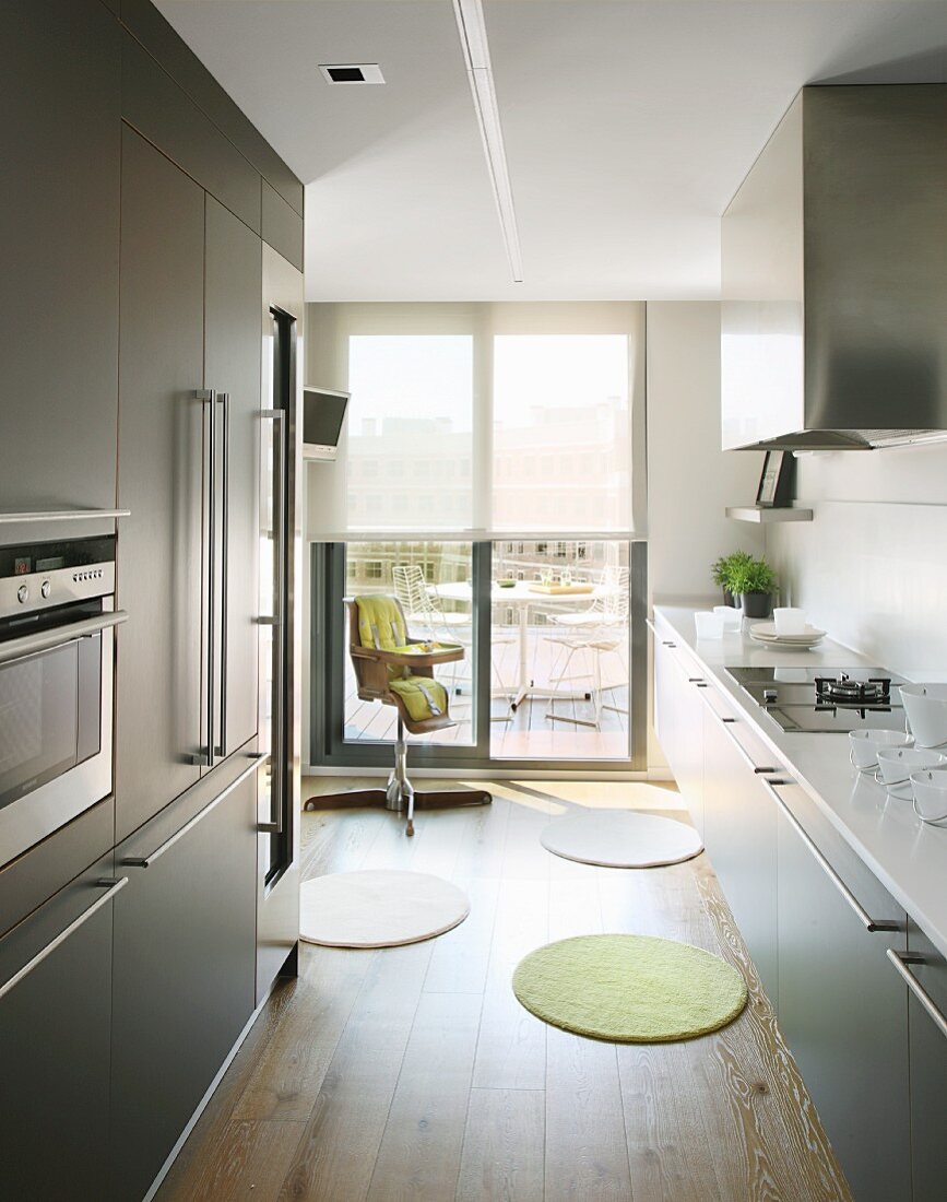 Modern kitchen with bar handles on grey cabinets along two walls; child's high chair in background in front of sliding door leading to roof terrace