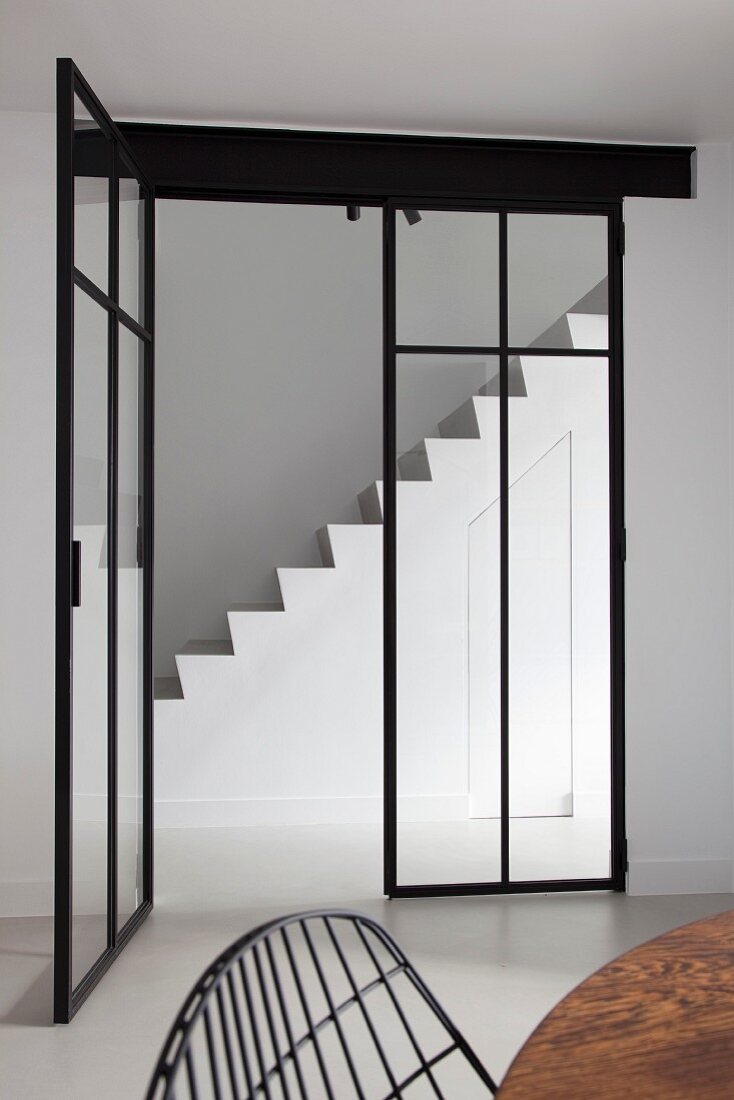 White masonry staircase with integrated storage in minimalist stairwell seen through glass and steel doors
