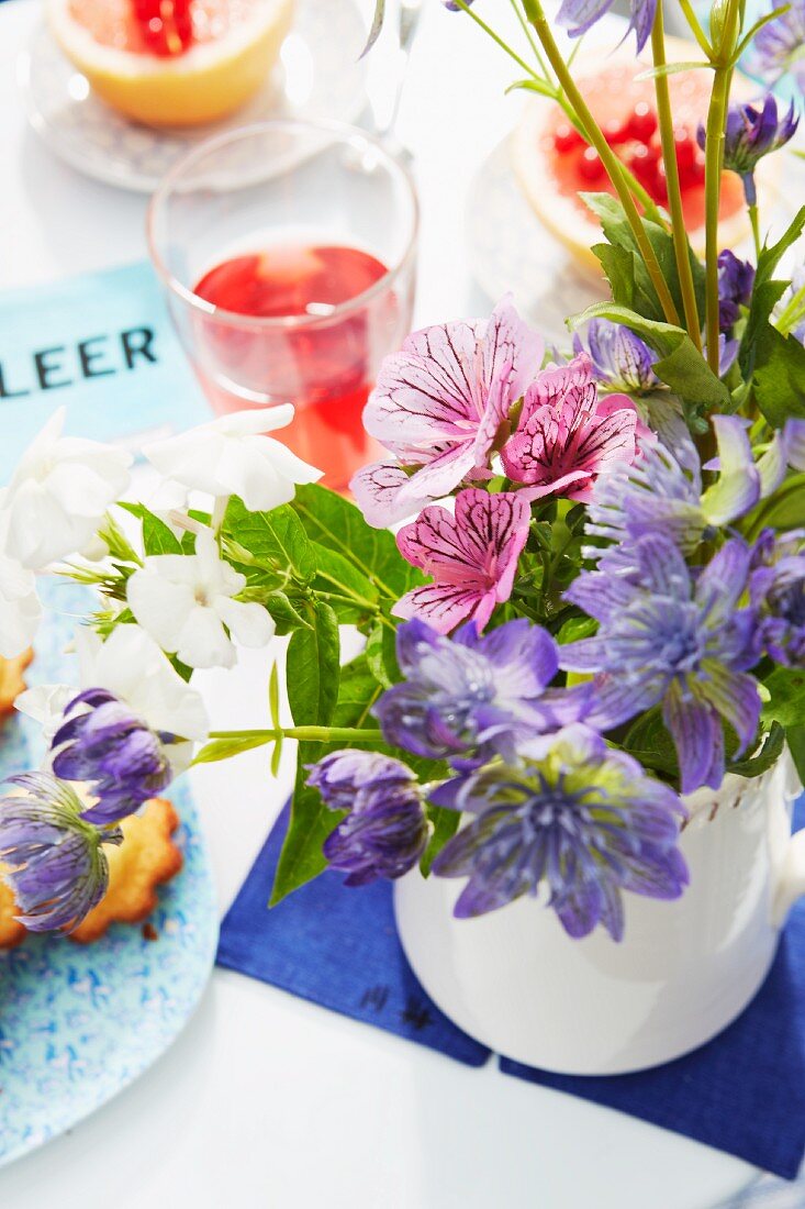 A bunch of delicate flowers, cakes and juice on a table laid on a summery balcony