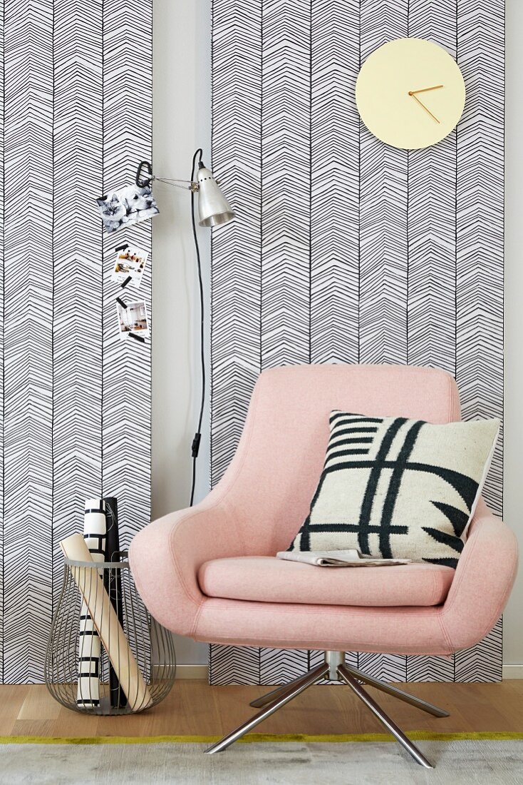 A pastel pink swivel chair contrasting with the geographic black-and-white patterns on the wallpapered wooden panels and cushion