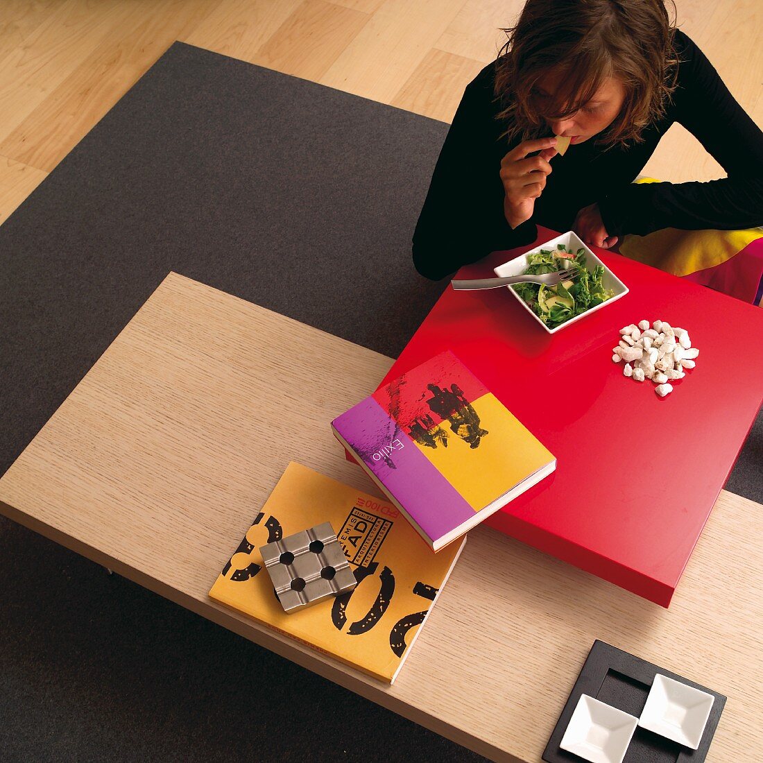 Woman eating at low table with red tabletop above wooden surface