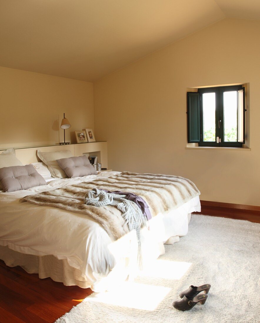 Doppelbett mit Fell Tagesdecke und weiße Bettwäsche in minimalistischem Schlafzimmer unter dem Dach