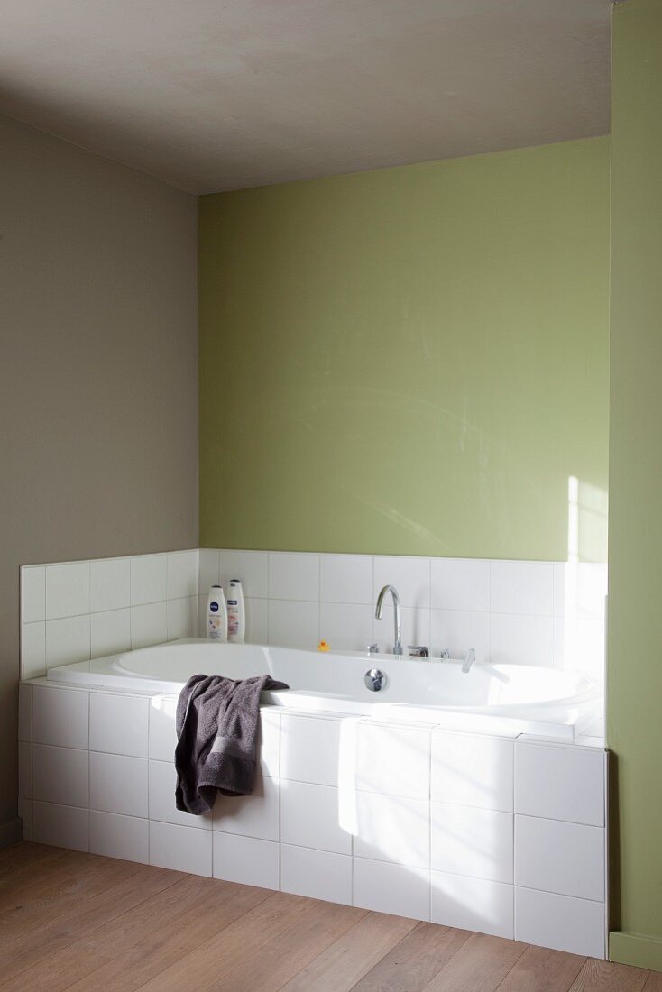Fitted bathtub with white-tiled front in niche with green-painted walls