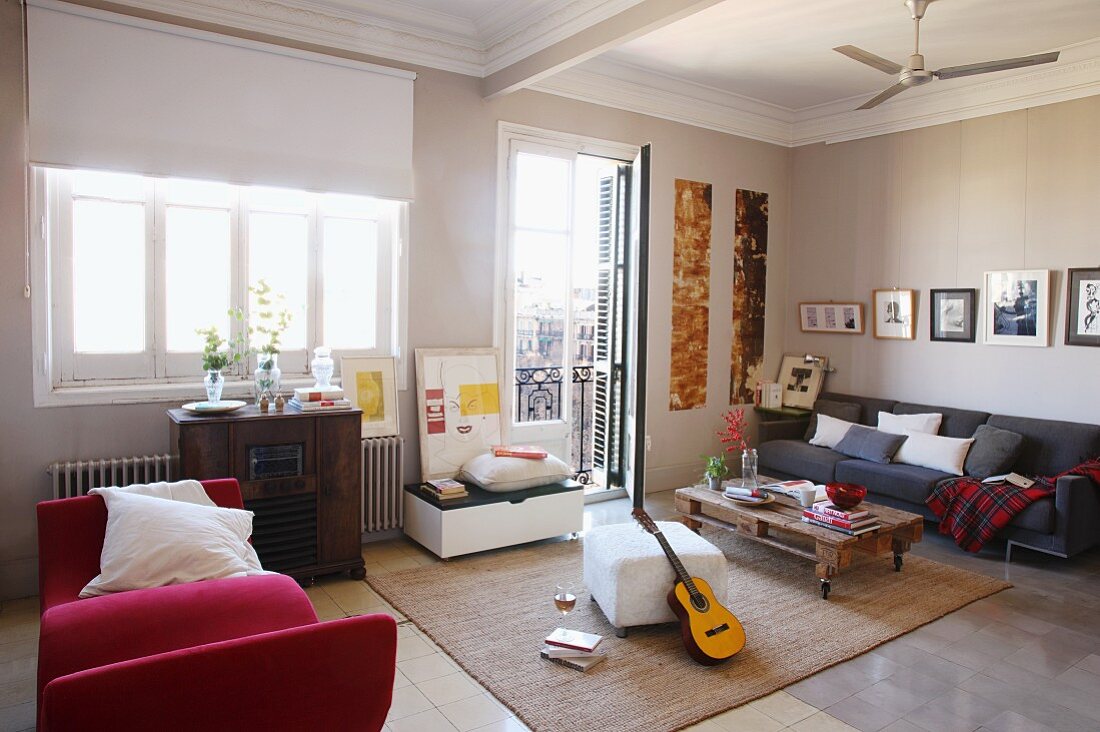 Moderne Möbel, rote Polsterliege, weisser Hocker und Bodentisch auf Rollen vor Couch in grossräumigem Wohnzimmer mit traditionellem Flair