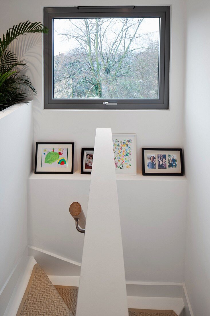 View down stairwell with view through window above framed photos on shelf