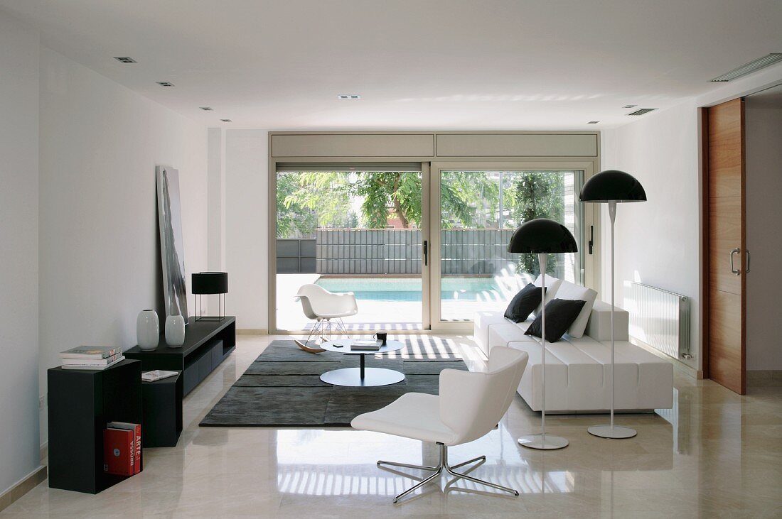 Modern living room in black and white; white swivel chair and standard lamps with mushroom-shaped lampshades next to contemporary sofa