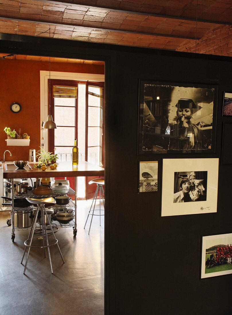 Blick vorbei an schwarzer Trennwand mit Erinnerungsfotos auf Metall-Barhocker an Frühstückstheke in der Küche