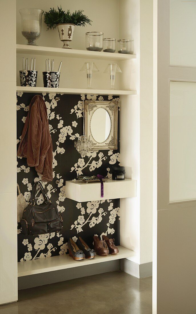 In Wandnische integrierte Garderobe mit floraler, schwarz-weisser Tapete und Glasdeko auf Regalborden