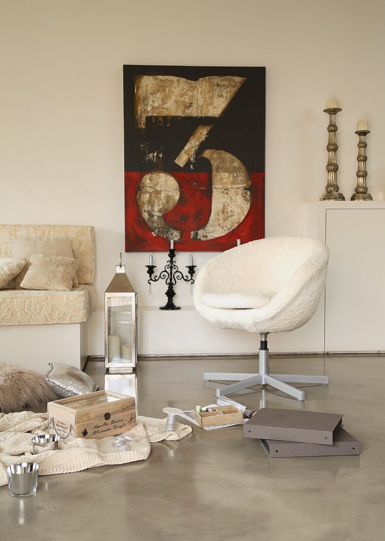 Collection of objects on polished concrete floor in front of retro swivel chair, modern printed artwork and candlesticks on shelves