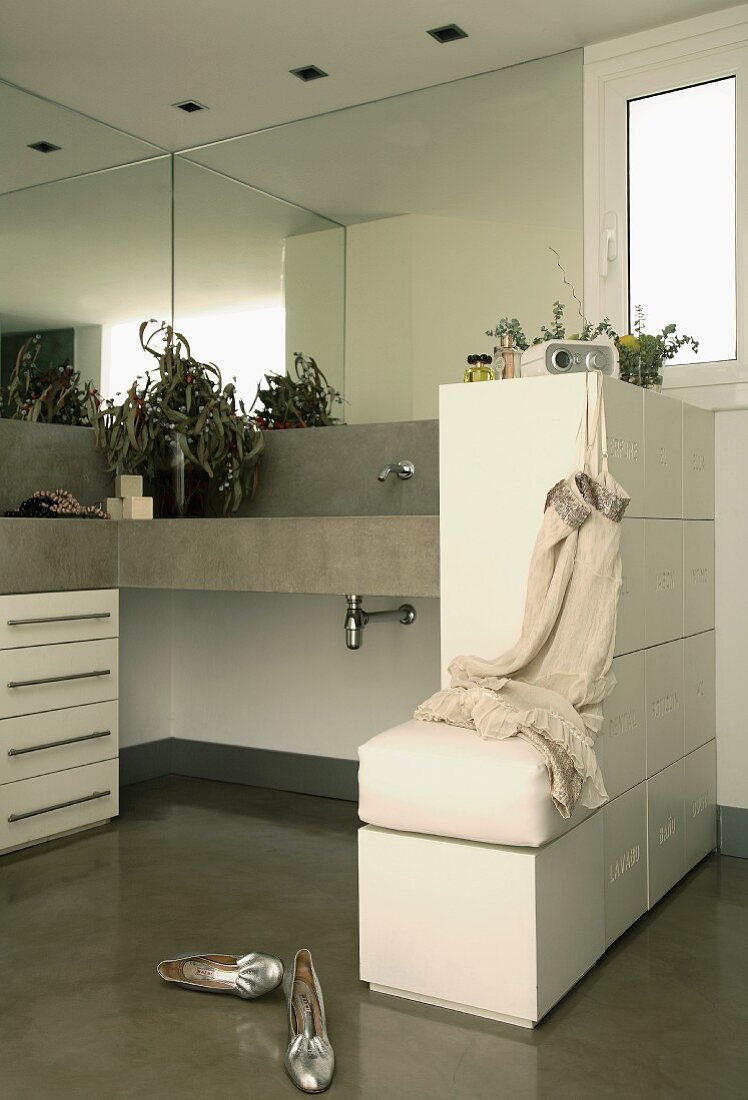 Beton-Waschtisch, übereck mit Spiegelfront und Unterbauschrank; seitlich ein halbhoher Raumteiler mit Tipp-On-Schubladen und Ablage-Hocker