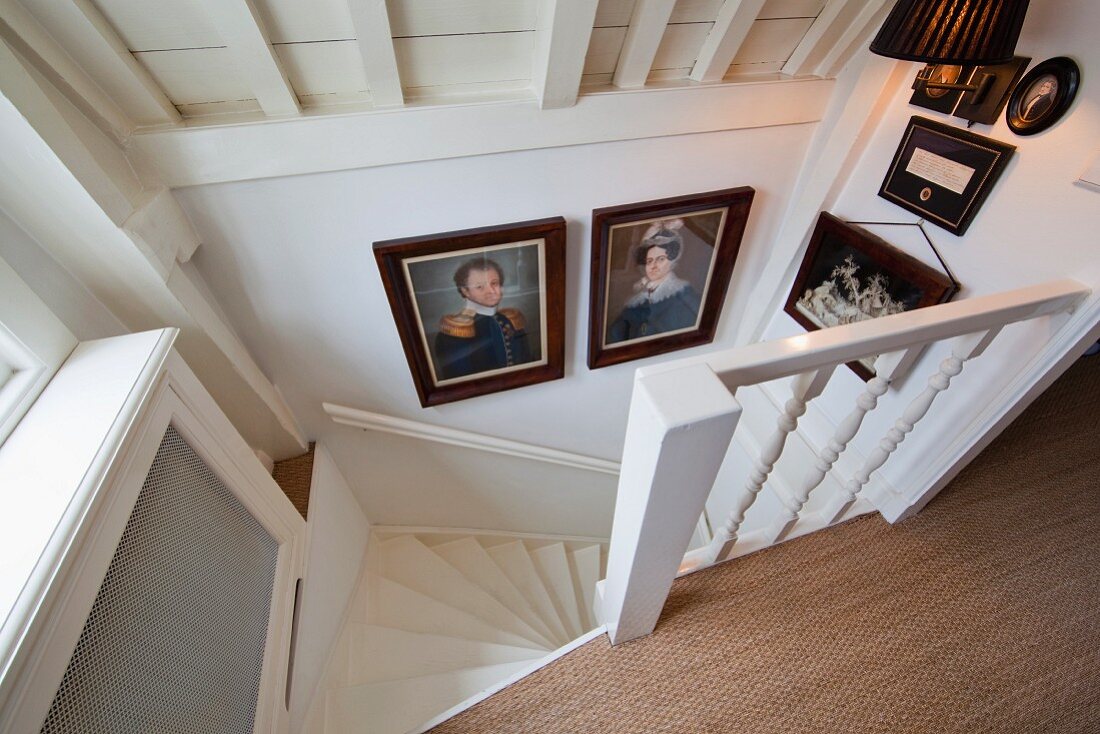 Blick von oben auf historische Bilder im Abgang einer gewendelten Landhaustreppe