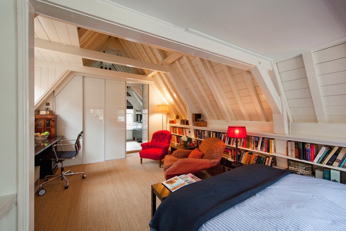 Multifunktionales Dachzimmer mit Homeoffice, Sitzecke vor Bücherregalen und Bett unter offener, weiss lackierter Holzkonstruktion