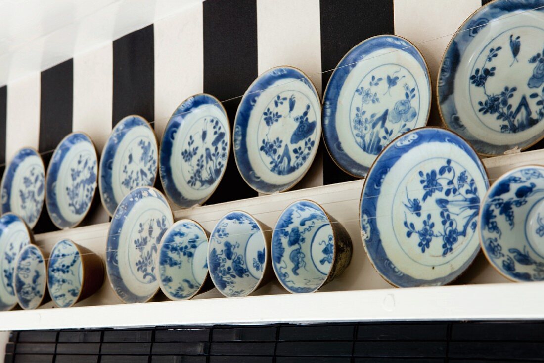 Sammlung blau-weisser Teller und Schalen auf Holzbord vor Blockstreifentapete
