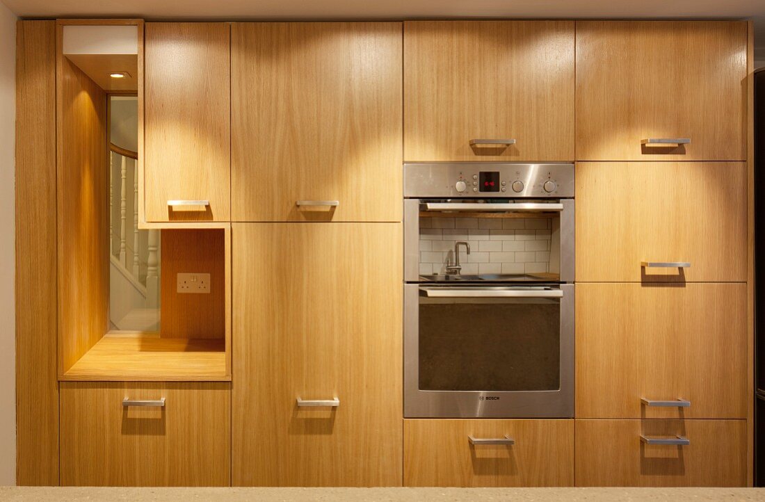 Küchenschrank mit Holzfront und Edelstahl Möbelgriffen, Kücheneinbaugeräte, seitlich integrierte Öffnung mit Blick auf Treppe