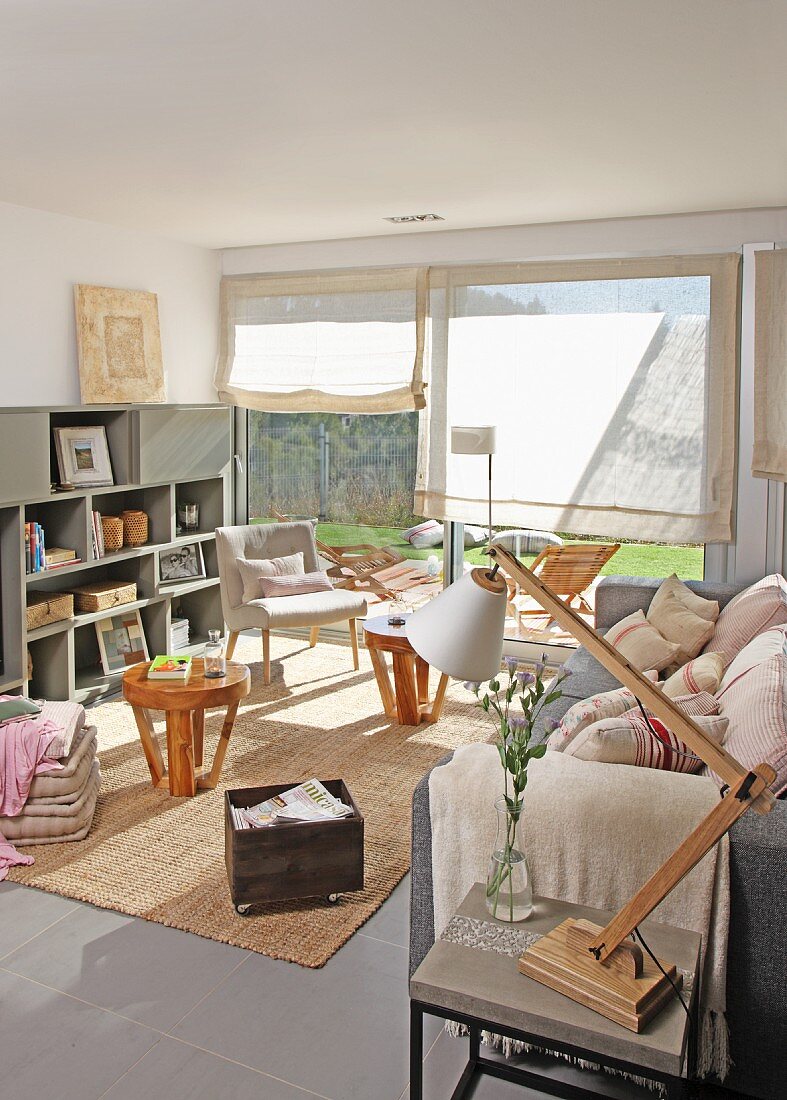 Auf Beistelltisch verstellbare Tischleuchte neben Sofa, runde Holz Beistelltische und Sessel in Loungebereich vor Fenster
