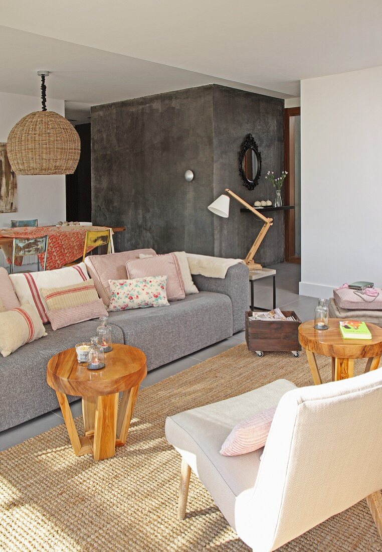 Graue Couch um runde Holz Beistelltische auf Sisalteppich in Loungebereich in offenem Wohnraum