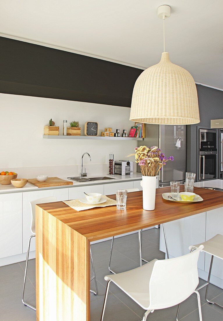 Pendant lamp with wicker lampshade above dining table and bar stools in open-plan designer kitchen
