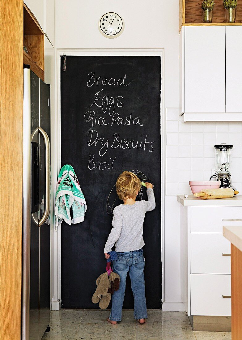 Young child drawing on chalkboard door