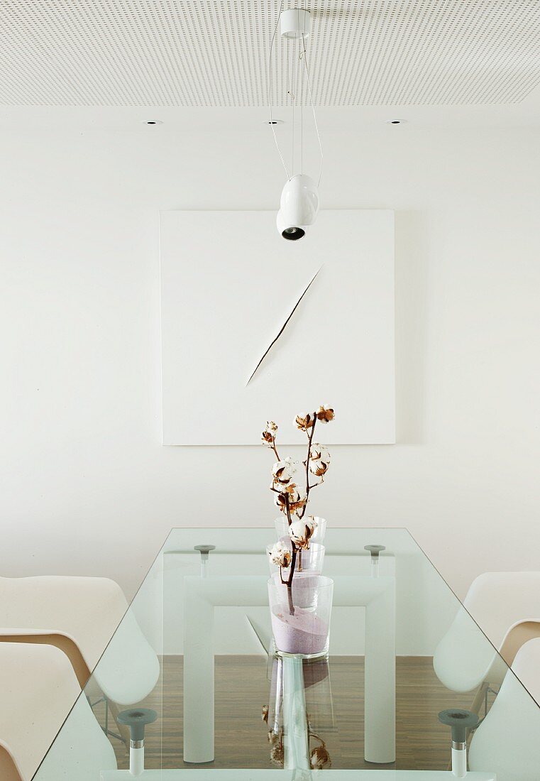 Zweige mit Baumwollblüten in sandgefüllten Vasen auf Designer Glastisch, Klassikerstühle und modernes, weisses Bild an der Wand