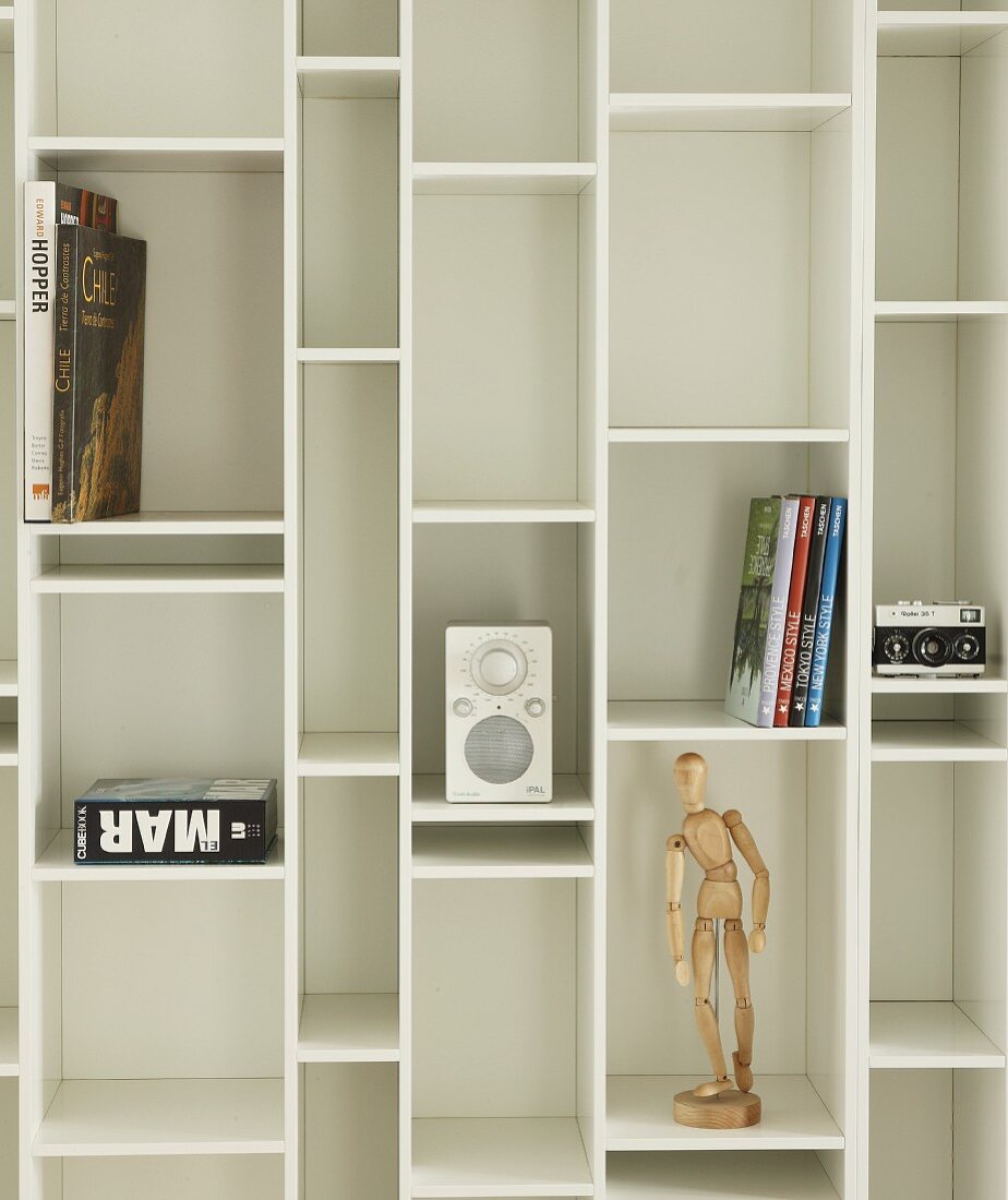 Books, jointed doll and small hifi on white fitted shelving with compartments of different sizes