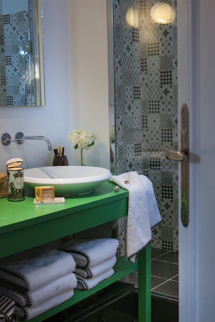Blick auf grün lackierten Waschtisch mit Aufbaubecken, seitlich Duschbereich mit schwarz-weiss gemusterten Wandfliesen
