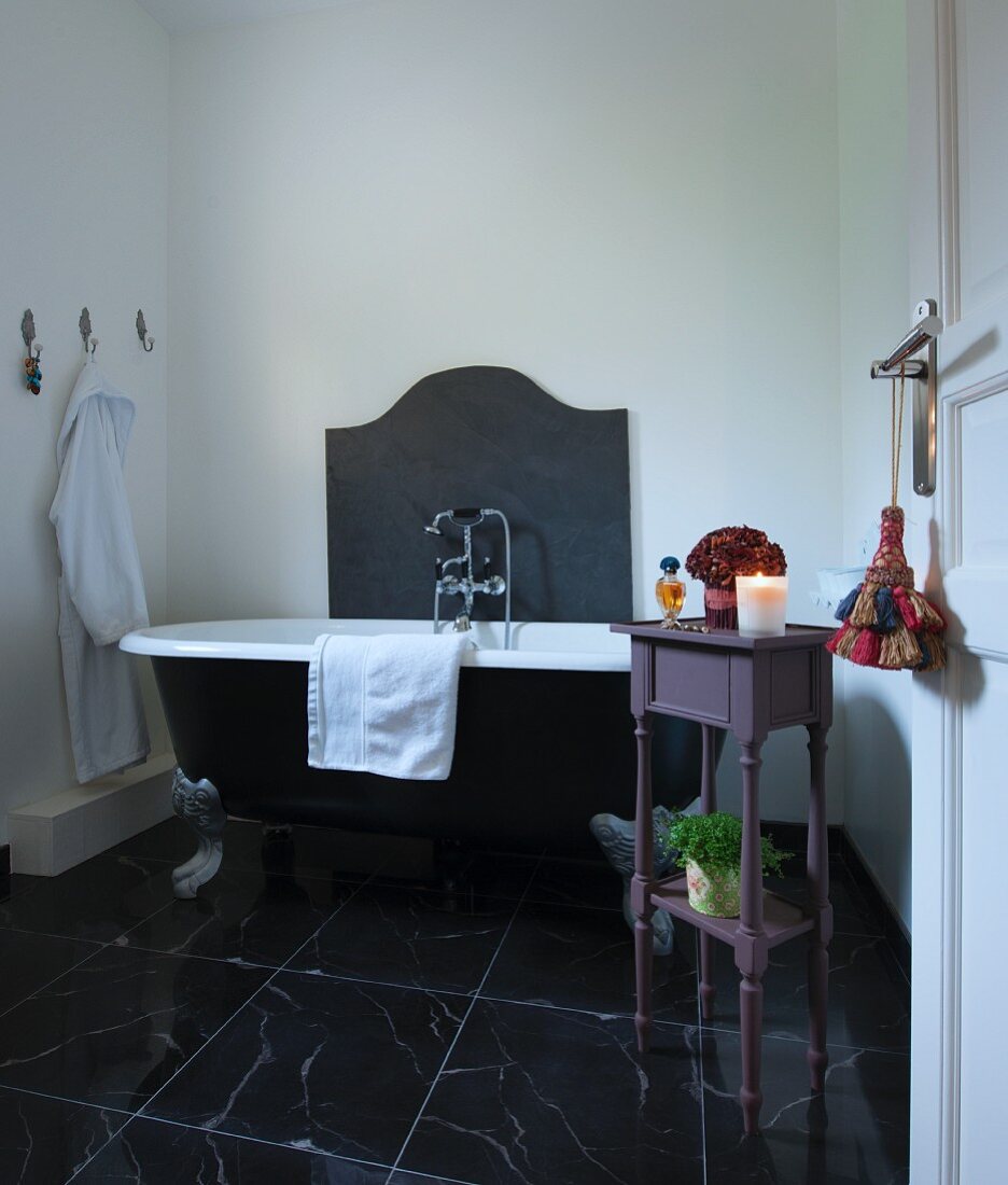 Wanne mit Klauenfüssen und Tischchen als Ablage im Badezimmer mit schwarzem Marmorboden