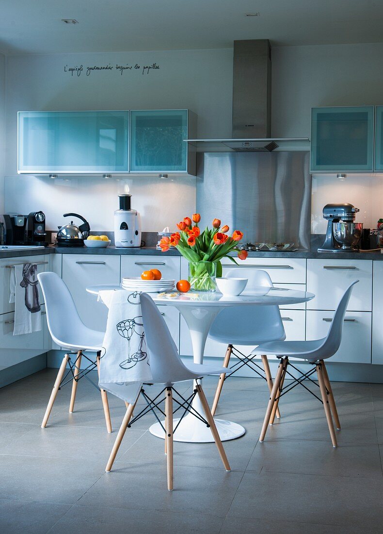 Moderne Küche mit weisser Schrankfront, in der Mitte Tulip Table mit Stühlen
