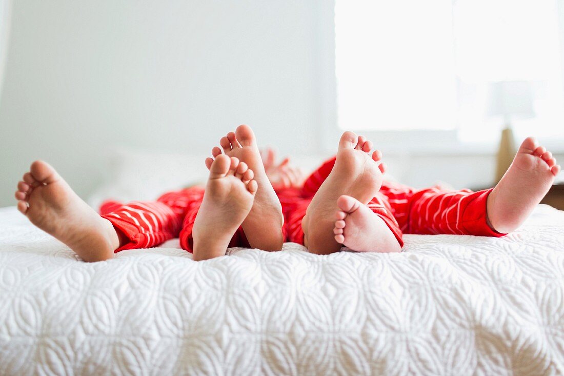 Geschwister in roten Pyjamas liegen auf dem Bett