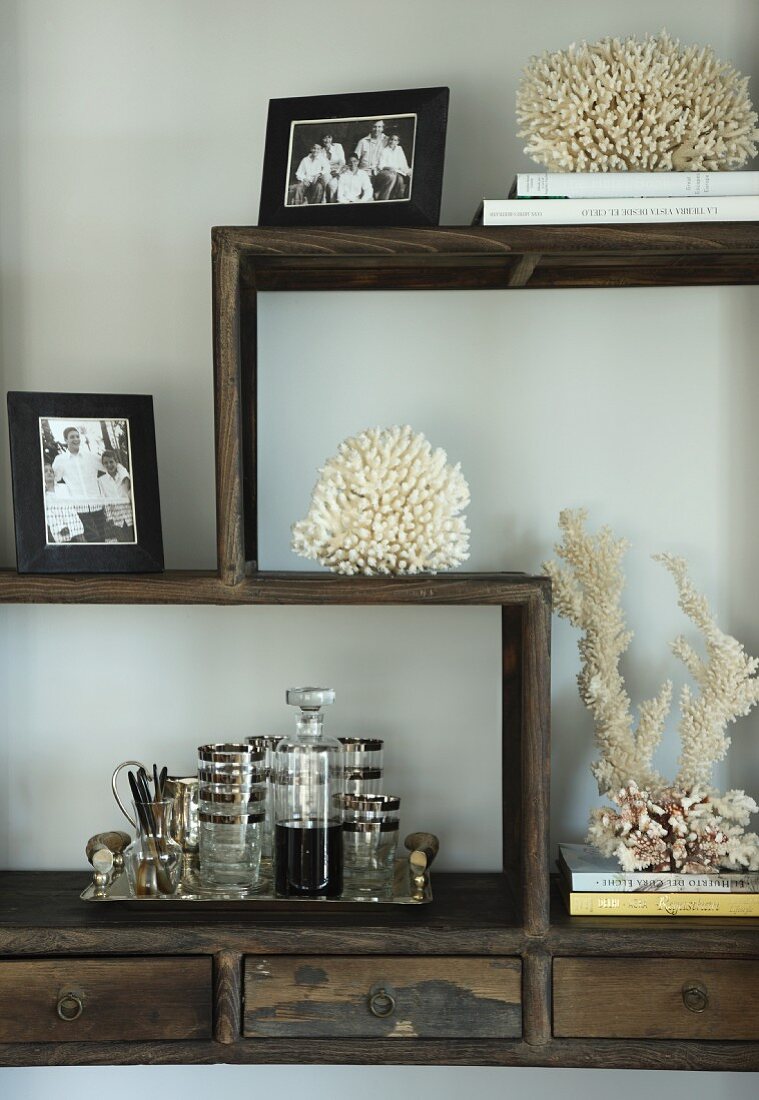 Coral, family photos and drinks tray on wooden cabinet with meandering shelving elements