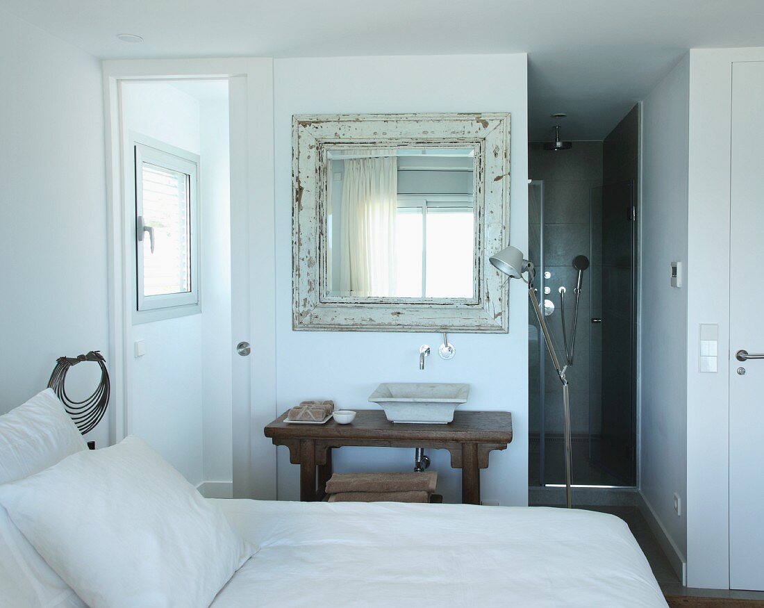 Blick über Bett auf rustikalem Waschtisch unter gerahmtem Vintage Spiegel, seitlich Tolomeo Stehleuchte im Schlafzimmer