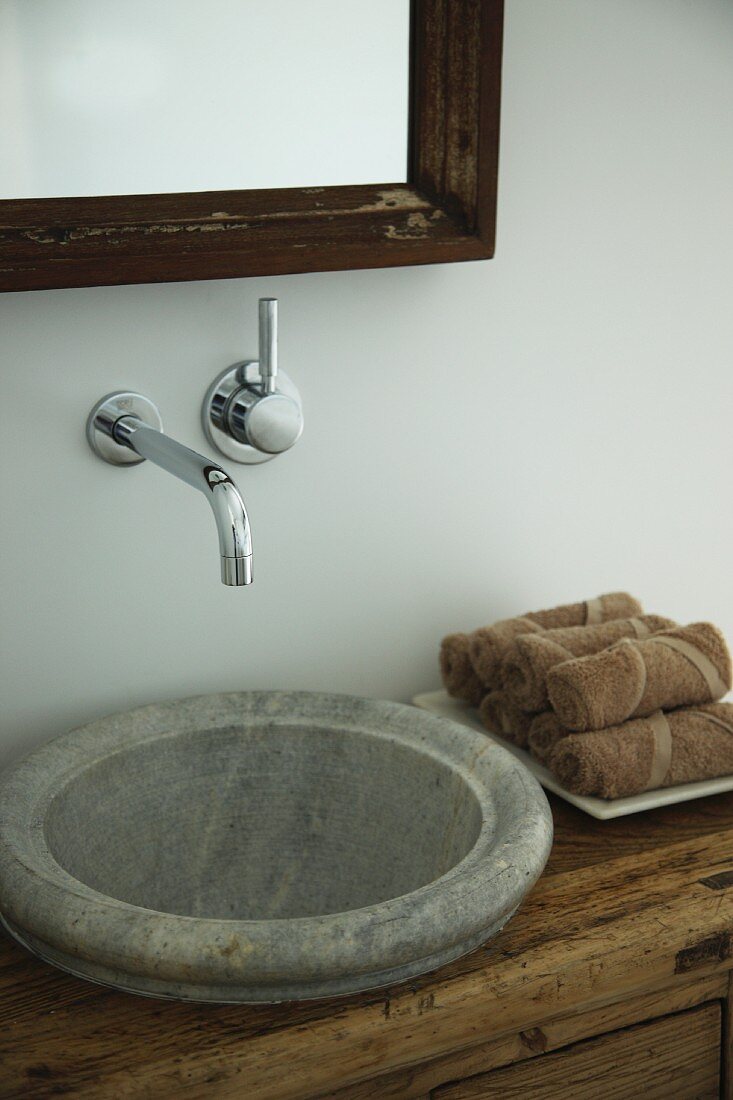 Rustic stone sink integrated into wooden chest of drawers with designer, wall-mounted taps