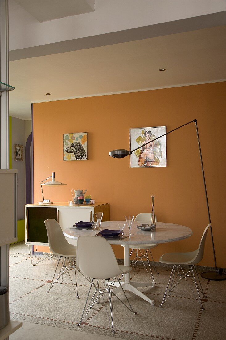 Esszimmer mit Designklassikern: runder Esstisch und Plastikstühle vor orangener Wand