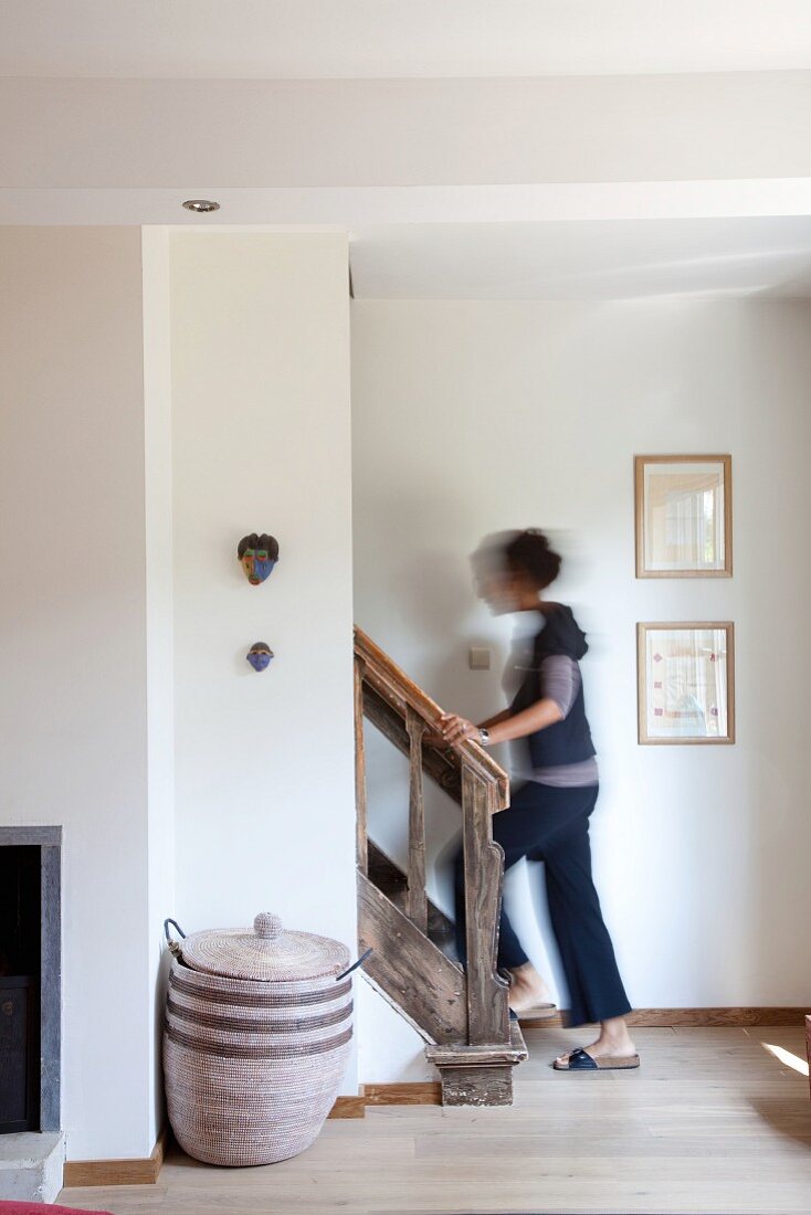 Woman walking up vintage wooden staircase; basket to one side