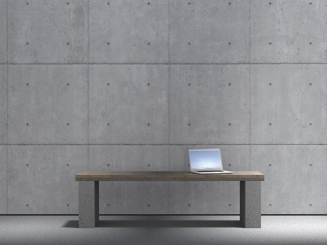 Laptop auf einer Bank aus Holz und Stein vor Sichtbetonwand mit quadratischen Fertigteilen