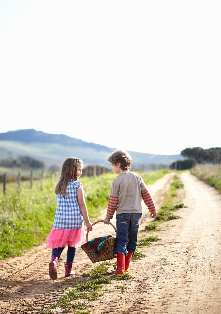 Zwei Kinder mit Picknickkorb auf einem Feldweg