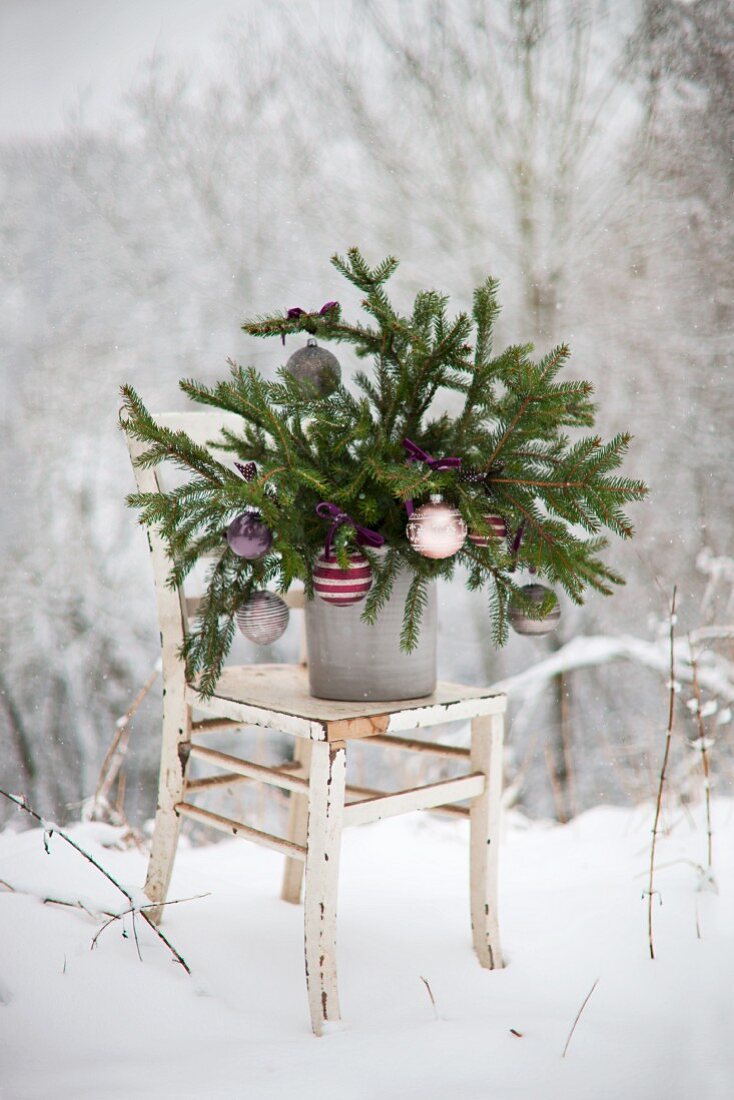 Fichtenzweige mit Christbaumkugeln dekoriert auf einem Shabby-Stuhl im Schnee