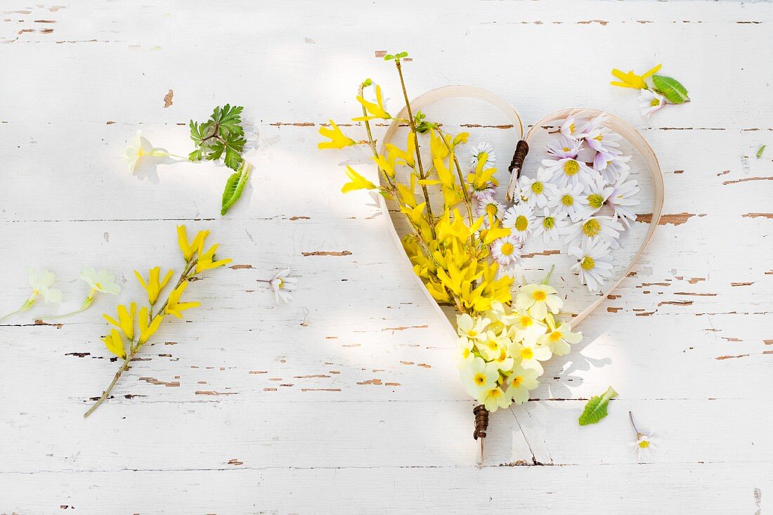 Frühlingsblumen in Dekoherz aus Spanholz geformt auf Holzuntergrund