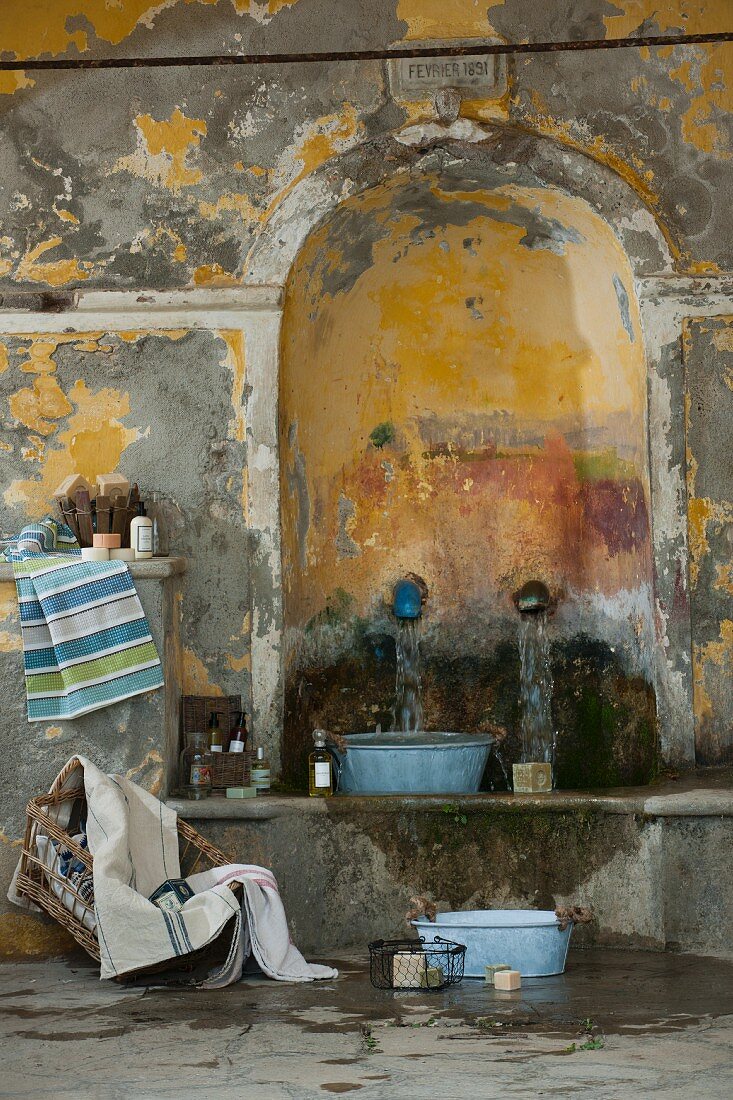 Waschbereich in Shabby Ambiente, Vintage Zinkwanne auf Steinbank unter Wasserspeier in Rundbogennische mit französischem mediterranem Flair