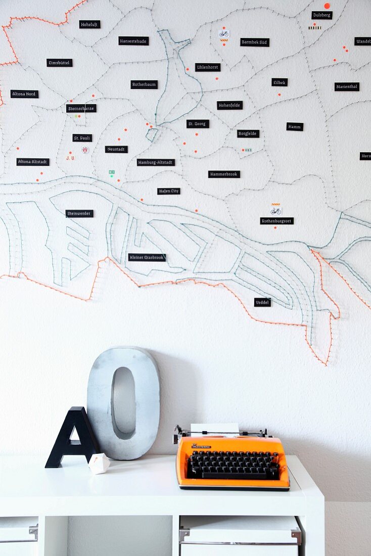 Stylised, string-art map of city decorating wall, orange retro typewriter and ornamental letter on white shelf