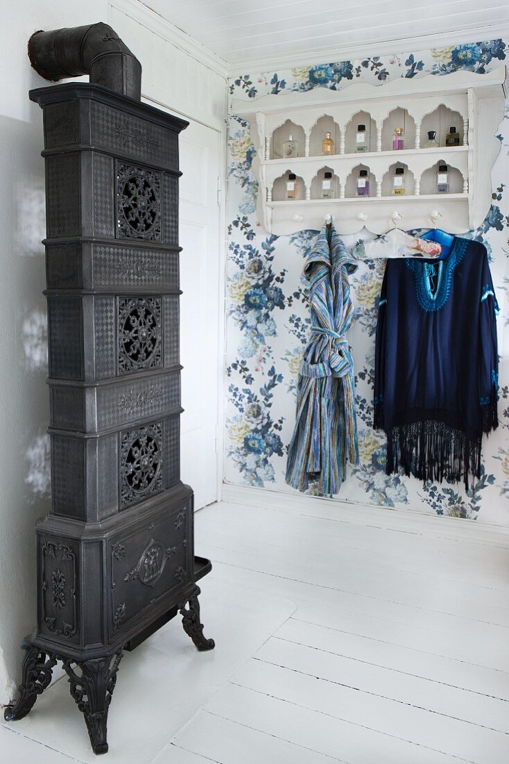 Antique, artistic stove and vintage-style shelves with coat hooks below on blue floral wallpaper