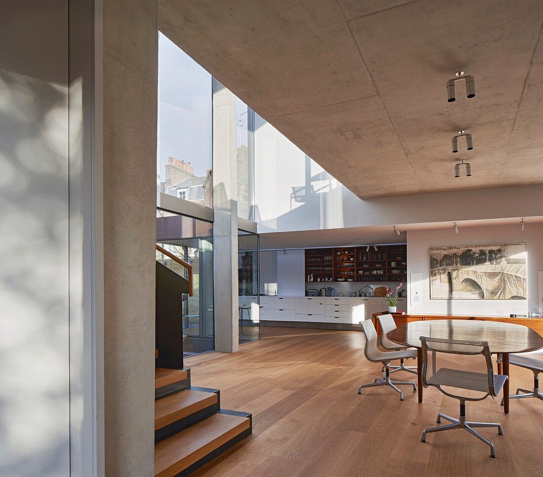 Offener Wohnraum mit Sichtbetondecke, Essplatz mit Klassikerstühlen, im Hintergrund Einbauküche, in zeitgenössischer Architektur